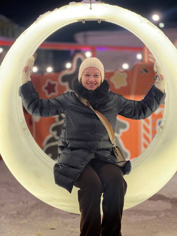 Улыбающаяся женщина сидит в круглом светящемся декоре на праздничной площади Рязани — вечерняя яркая иллюминация.