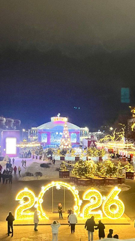 Общий вид на праздничную ярмарку Рязани с подсветкой и инсталляцией «2026»; люди гуляют по площади вечером.