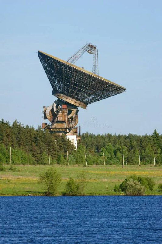 Радиотелескоп РТ-64 в окрестностях Калязина, огромная антенна на фоне леса и реки; индустриально-научный пейзаж под ясным небом.