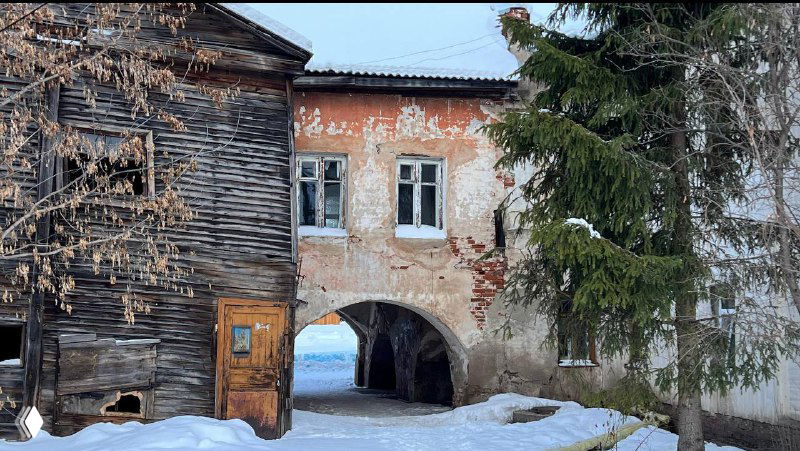 Старый деревянный дом с аркой и выцветшей фасадой, двор Углича с признаками возраста и исторического слоя.