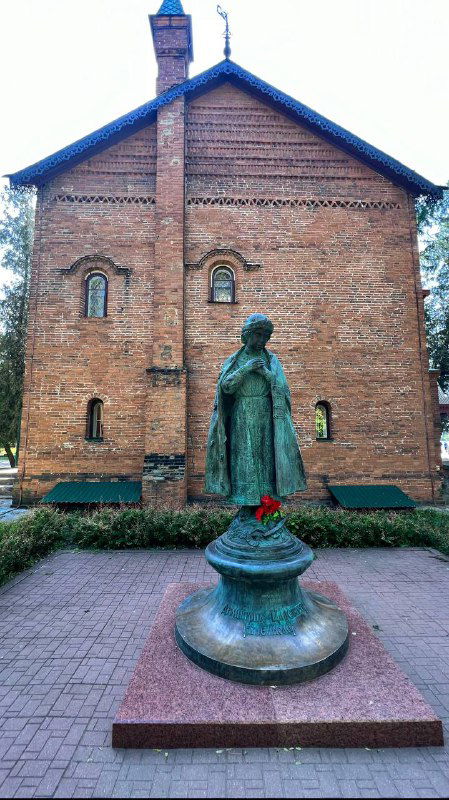 Памятник или статуя на фоне кирпичного здания в Угличе, спокойная композиция на городской площади.