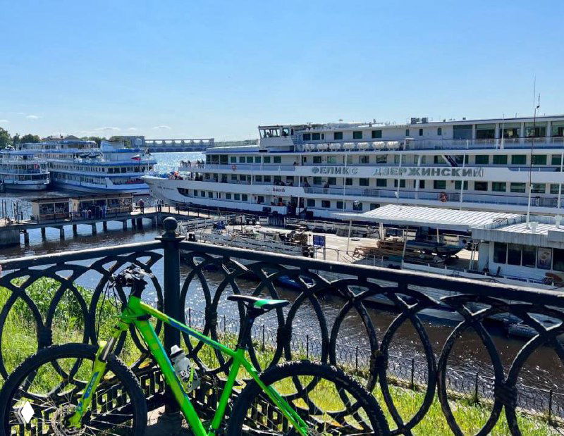Речная пристань и теплоходы в Угличе летом, вид через декоративное ограждение и велосипед в кадре, летняя навигация.