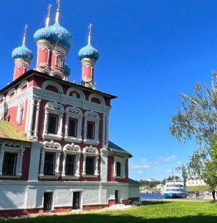 Фасад церкви в солнечный день, яркие краски и золотые купола, летний кадр с рекой на фоне.