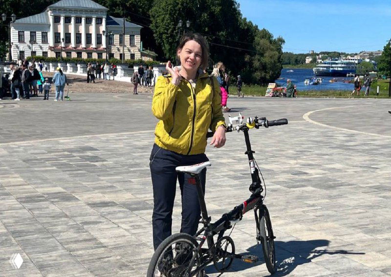 Человек с складным велосипедом на площади у набережной в солнечный день — прогулочная сцена и туристический образ.