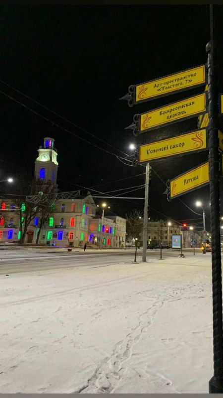 Ночная улица и указатели с подсветкой на фоне ратуши Витебска; снежная дорога и архитектурная иллюминация в кадре вечером.