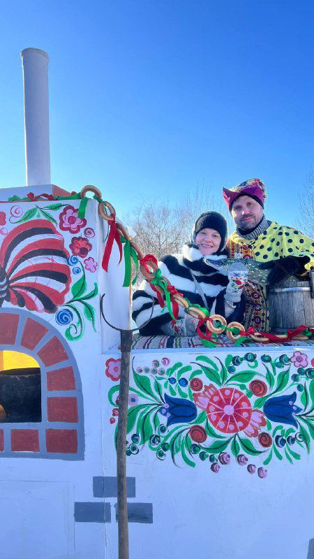 Интерактивная фотозона в стиле русской печи с раскрашенной росписью и улыбающимися людьми, создающая праздничное настроение.