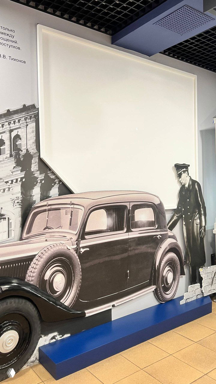 Интерактивный стенд с изображением ретро‑автомобиля и силуэтом в форме — музейный монтаж, который иллюстрирует кинематографическую эстетику и время ролей Тихонова.