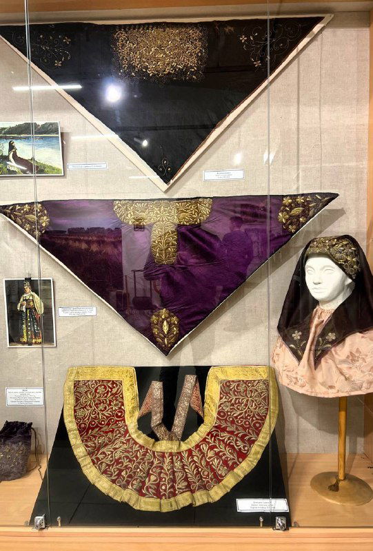 Треугольные шали и декоративные воротники в витрине музея: образцы разной формы и отделки, золотистые и бархатные вставки, манера оформления экспонатов.