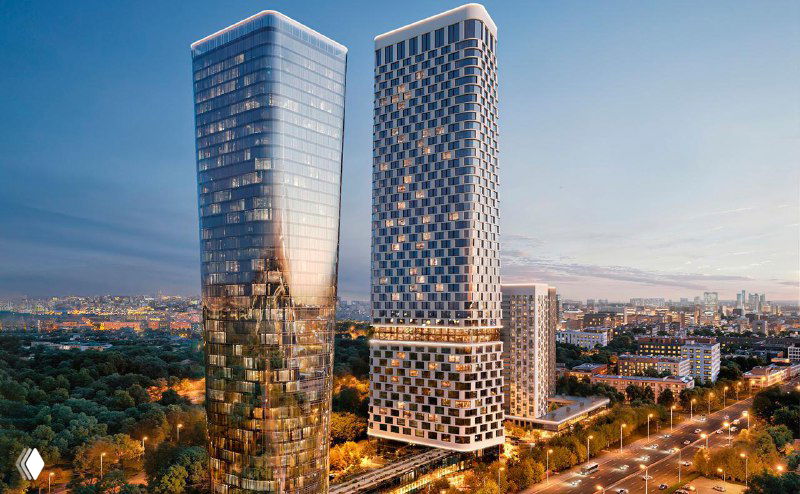 Общий вид ЖК Solos: две башни разной высоты рядом с парком Сокольники и городским ландшафтом на фоне заката.