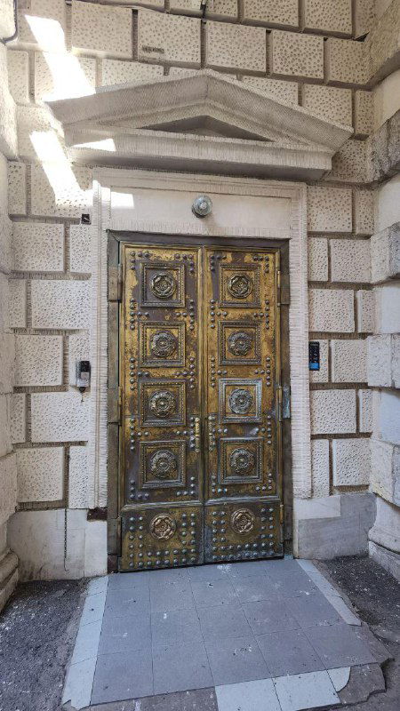 Тяжёлая декоративная парадная дверь с орнаментом и металлической отделкой — вход в жилую парадную доходного дома XIX века в Петербурге.