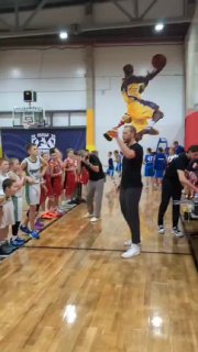 Динамичный игровой кадр: игрок в жёлтой форме совершает прыжок с мячом в попытке забросить мимо защитников на фоне трибун и баннеров.