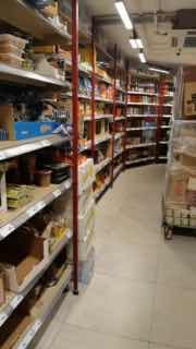 Узкие торговые проходы с металлическими стеллажами и частично заполнёнными полками; вид на организацию торгового пространства и складской запас.