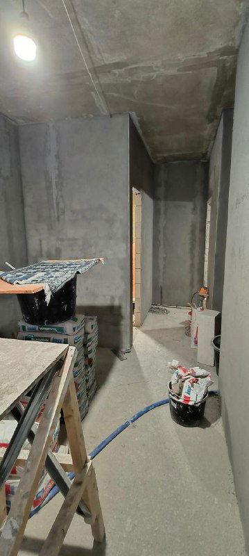 Черновые отделочные работы в комнате: выровненные стены со штукатурными маяками, строительные инструменты и материалы на полу у подготовленного проёма.