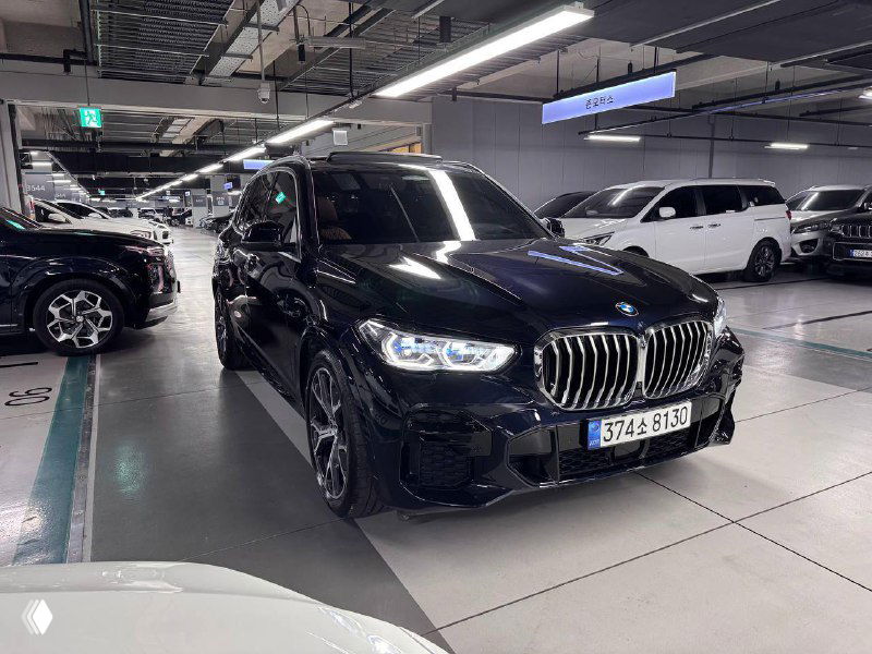 BMW X5 30d xDrive MSport в шоуруме, крупный план спереди слева, автомобиль на парковочном месте с отражениями потолочного освещения.