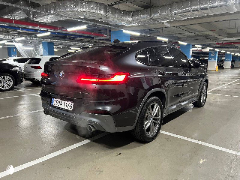 Задний ракурс BMW X4 в паркинге: тёмные кузовные панели и светящиеся задние фары, видно профиль и форму багажной двери автомобиля.