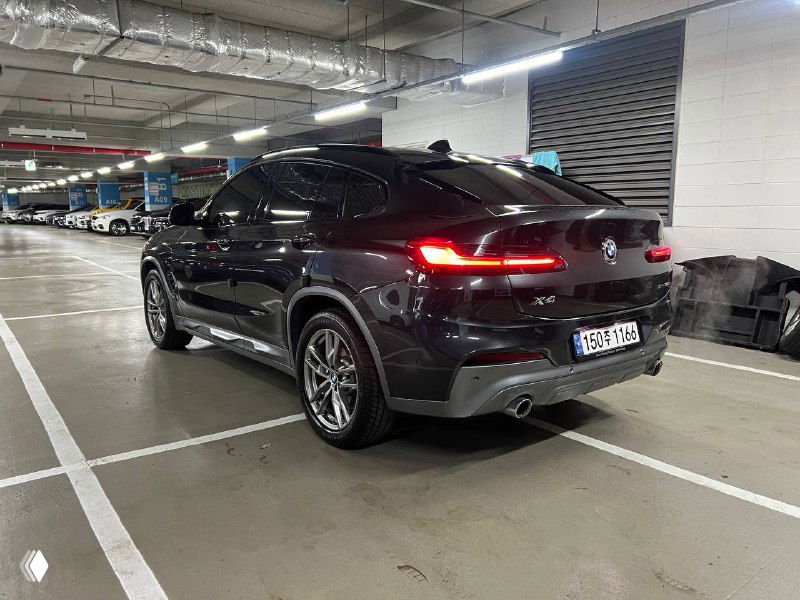 Косой ракурс задней правой части BMW X4 в подземном паркинге: колёса, бамперы и форма кузова под разным углом освещения.