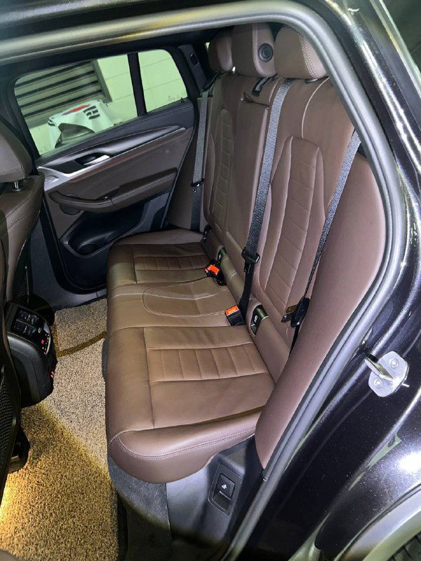 Задние сиденья BMW X4 в коричневой обшивке: состояние обивки, посадочные места и пространство для пассажиров, вид на салон с открытой дверью.