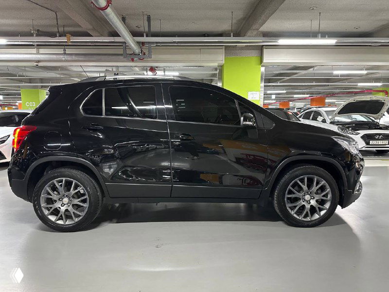 Боковой профиль черного Chevrolet Trax 2020 на стоянке, видны диски, линии дверей и отражения на лаке кузова.