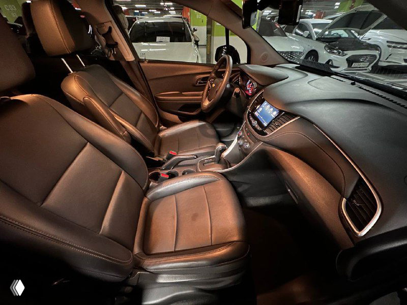 Передние сиденья и панорамный ракурс салона Chevrolet Trax 2020 — видно водительское и пассажирское кресла, руль и часть торпедо.