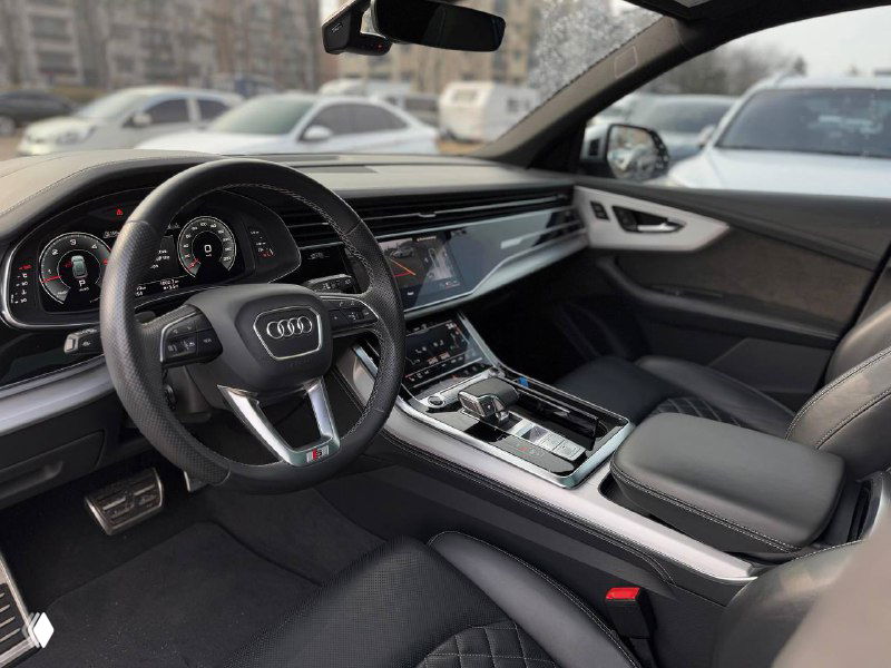 Вид на приборную панель и центральный дисплей Audi Q8, рулевое колесо, экран мультимедиа и элементы управления в салоне автомобиля.