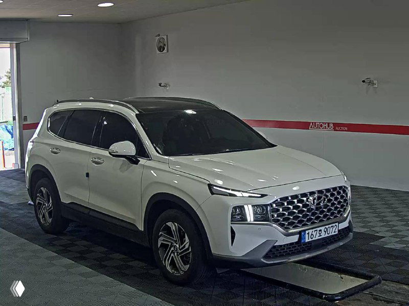 Hyundai Santa Fe с белым кузовом и чёрной крышей, общий ракурс в освещённом помещении, видна передняя левая часть автомобиля и колёса