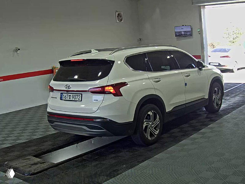 Задняя часть белого Hyundai Santa Fe в боковом ракурсе в боксе осмотра, видна оптика, багажная дверь и задний бампер