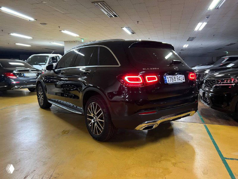 Задняя часть черного Mercedes GLC 220 D 4Matic в закрытой стоянке, светящиеся задние фонари и вид рельефа кузова на парковке.