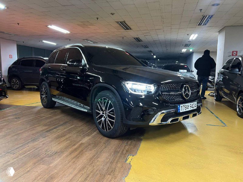 Черный Mercedes GLC 220 D 4Matic на стоянке, крупный план фары и решетки радиатора, вид сбоку‑спереди с отражениями потолочного света.