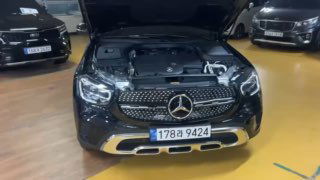 Открытый капот Mercedes GLC 220 D 4Matic в паркинге, вид на моторный отсек и переднюю часть автомобиля с номером на бампере.