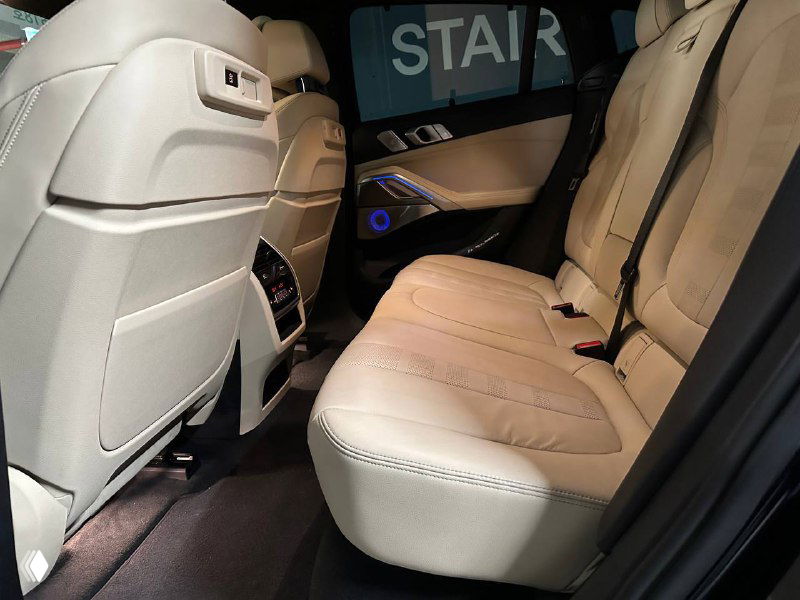 Задний ряд сидений BMW X6 в светлой кожаной обивке, пространство для ног и задняя часть передних сидений видны в реальном освещении паркинга