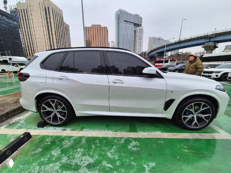 Белый BMW X5 30D, боковой общий план: видны колёсные диски M Sport, высокая линия крыши и затемнённые задние стёкла на парковке.