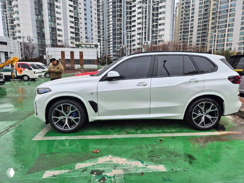 Белый BMW X5 30D, боковой крупный план на парковочном месте; видна линия порога, отражения городской застройки и снежные следы на асфальте.