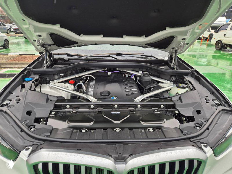 Вид под открытым капотом BMW X5 30D: моторный отсек, распорки и заводские элементы — чистый моторный отсек на демонстрационной парковке.