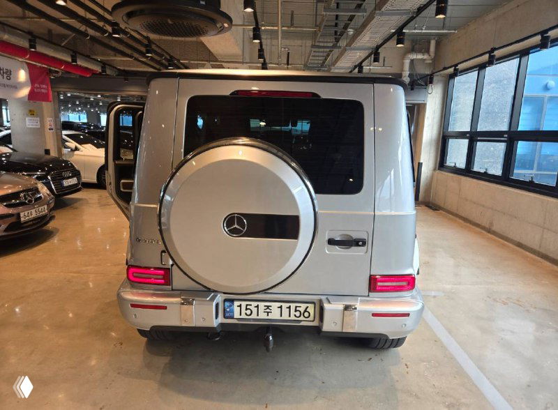 Задняя часть Mercedes G‑Class серебристого цвета: запасное колесо на двери, задние фонари и общая длина кузова на парковке