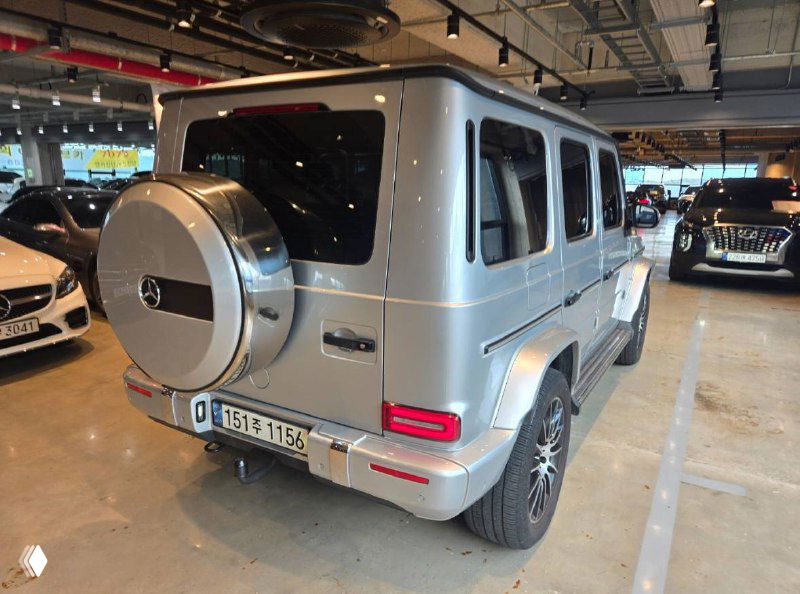 Угловой ракурс задней части Mercedes G‑VAGEN, видно профиль заднего крыла, фонари и соседние машины в паркинге