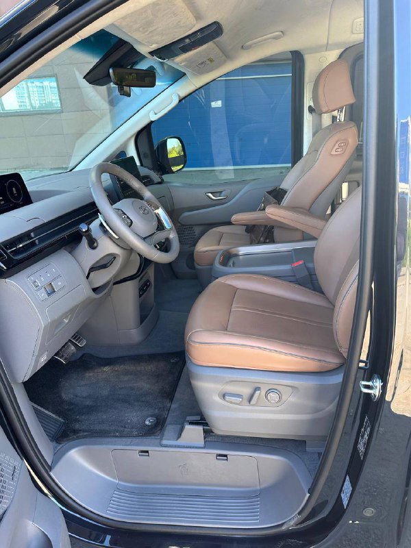 Водительское сиденье Hyundai Staria в коричневой коже, видны электрорегулировки и отделка, дверь открыта для обзора салона.
