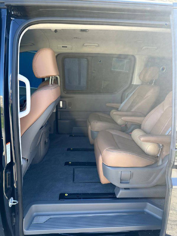 Вид в салон Hyundai Staria через открытую боковую дверь, показаны проход и ряд сидений, чистый пол и направляющие для кресел.