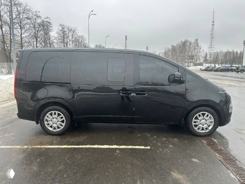 Боковой профиль Hyundai Staria Cargo чёрного цвета на парковке; видно сдвижную дверь и ровную боковую панель автомобиля-универсала.