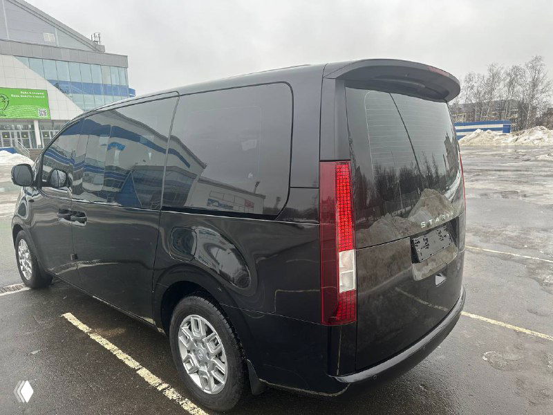 Задняя часть Hyundai Staria Cargo чёрного цвета; открыт доступ к багажнику, видна форма фонарей и общая компоновка кормы автомобиля.