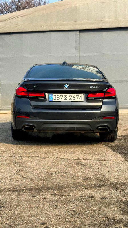 Задний вид чёрного BMW 540i xDrive M Sport: багажник, фонари и диффузор на парковке, общий вид задней части машины.