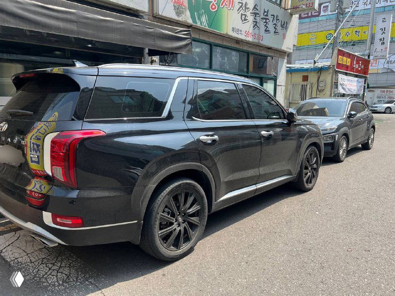 Боковой ракурс Hyundai Palisade Prestige чёрного цвета на улице, крупные колёсные диски и профиль кузова, общий городской фон.