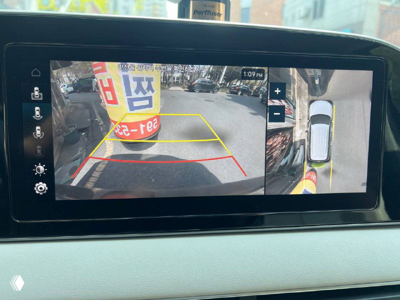 Экран мультимедиа Hyundai Palisade Prestige отображает изображение с камеры заднего вида и схему парковки, видно разметку и боковой обзор.