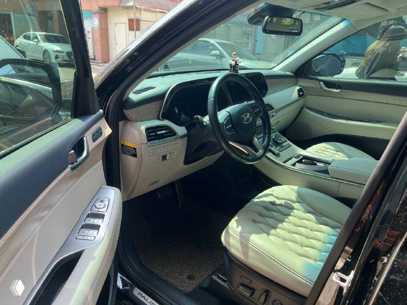 Передняя часть салона Hyundai Palisade Prestige: водительское место, центральная консоль и передние сиденья с обивкой светлого цвета.