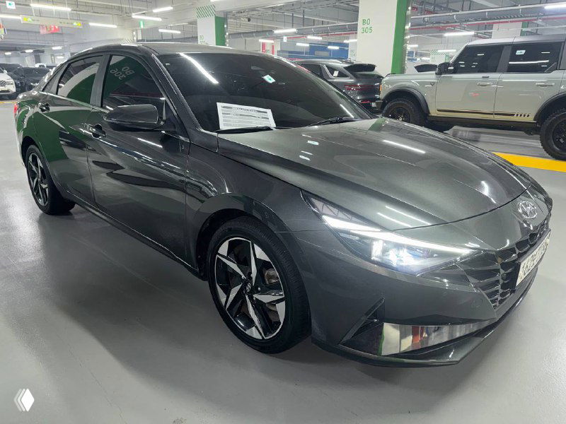 Серый Hyundai Avante, вид спереди под углом, подчёркнут дизайн фальшрадиаторной решётки и передней оптики, парковка дилерского центра.