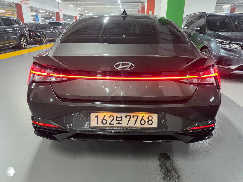 Задняя часть Hyundai Avante с корейским номером 162보7768, снимок в паркинге показывает сплошную световую полосу и состояние бампера.