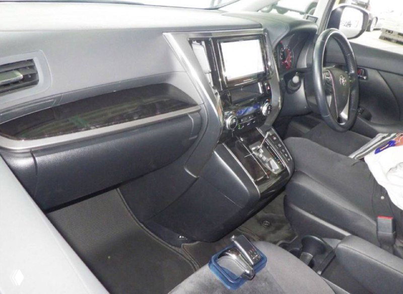 Интерьер Toyota Alphard: приборная панель и центральная консоль с мультимедийным экраном, селектор передач и часть переднего пассажирского места.