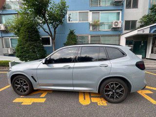 Боковой профиль BMW X3 20i xDrive M Sport Pro с белым кузовом, тёмными дисками и тонированными стеклами; фото со стороны водителя на парковке.