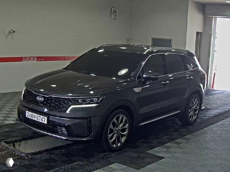 Kia Sorento 2.2 дизель, фронтальный ракурс с водительской стороны на парковочной площадке, отражения и освещение автосервиса.
