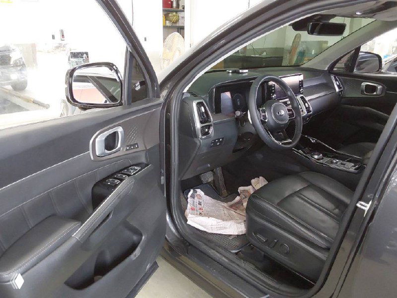 Передняя дверь и водительское место Kia Sorento 2021, вид со стороны открытой двери, кожаное сиденье и органы управления на двери.