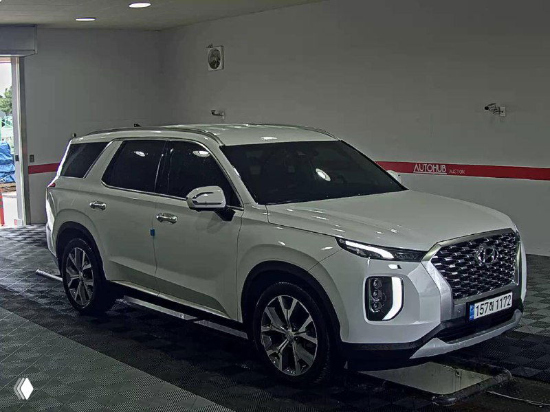 Hyundai Palisade белого цвета, вид спереди-сбоку в автосалоне, заметны боковые панели, диски и общий внешний вид автомобиля.